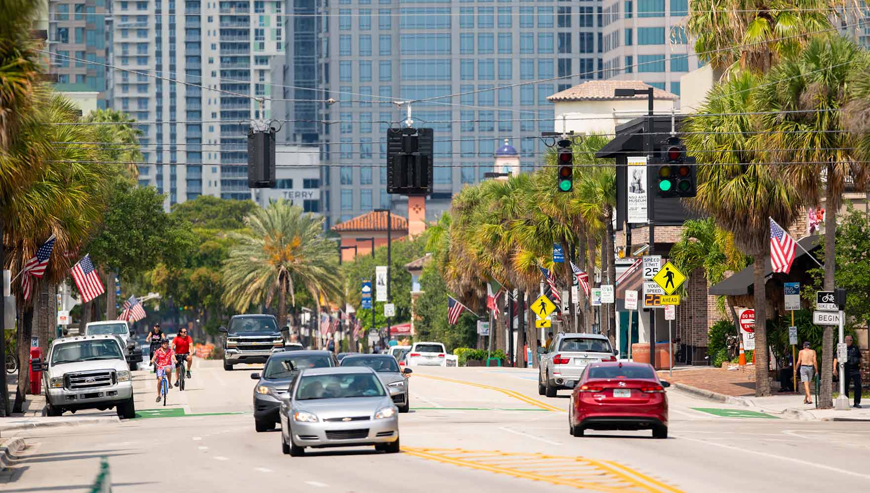 A busy urban street with cars, palm trees, and tall buildings in the background.