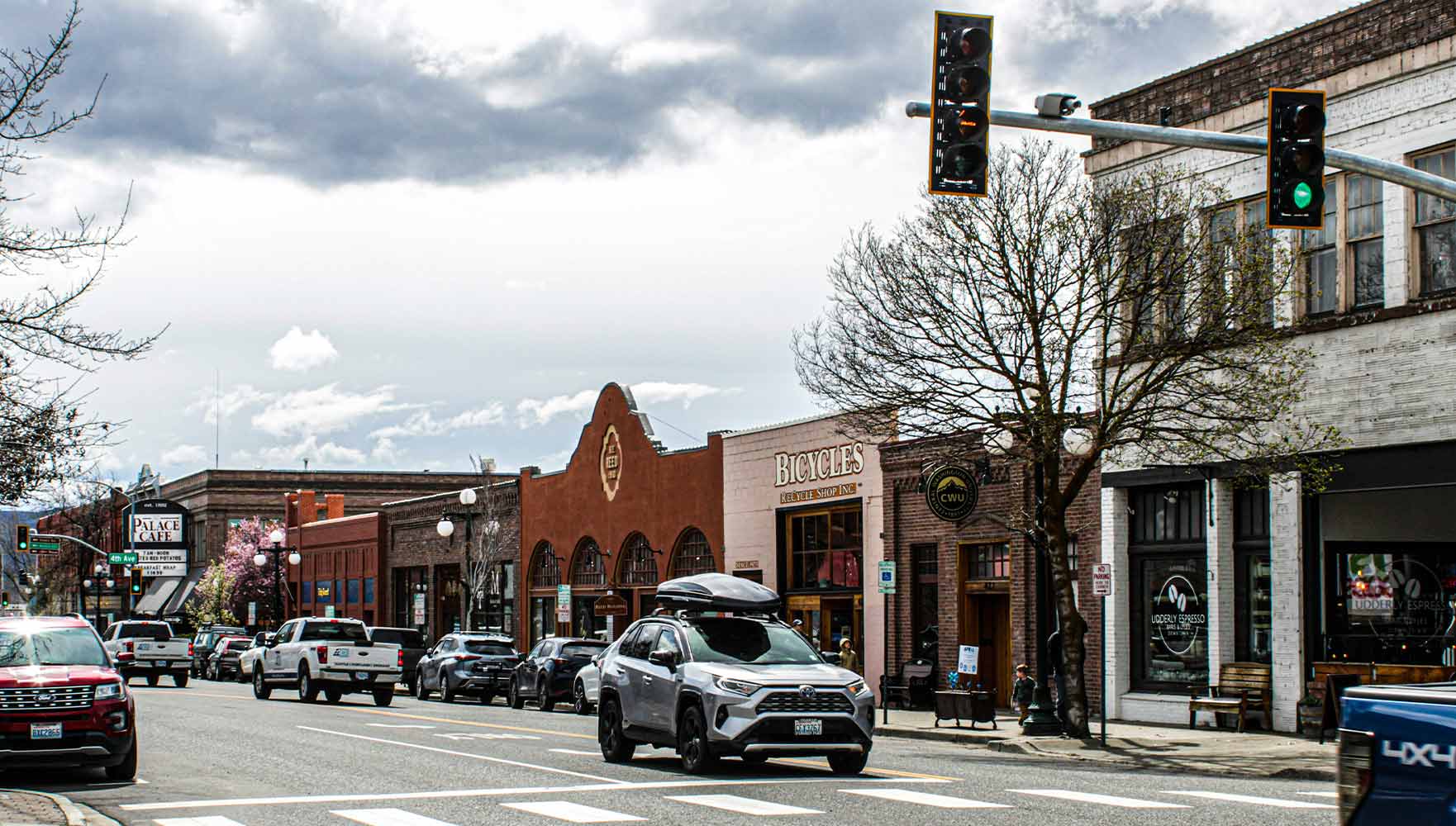 Downtown street with historic buildings, cars, pedestrians, and traffic lights on a cloudy day.